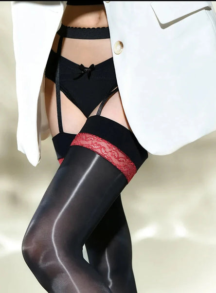 A woman posing in a black glossy thigh high stockings with red lace details, and attached garter straps.