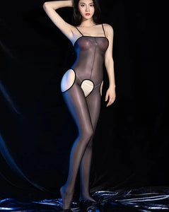 A woman posing in a black glossy sheer suspender bodystocking with spaghetti straps, and an open crotch.