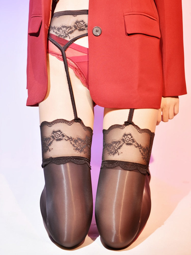 A woman posing in a black glossy thigh high stockings, with an attached garter belt with floral embroidery. 