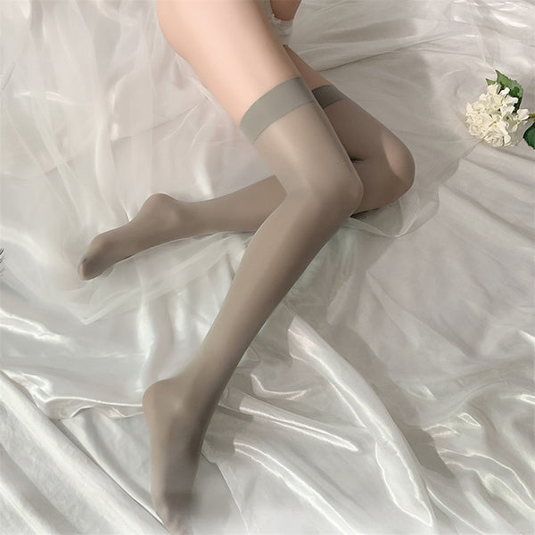 Side of lady wearing a gray shiny sheer thigh-high stockings, featuring a gray color wide band, showing off her feet.